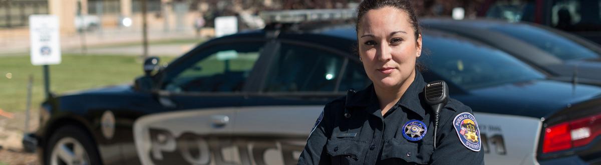 Female Law Enforcement Academy graduate standing in uniform in front of police car