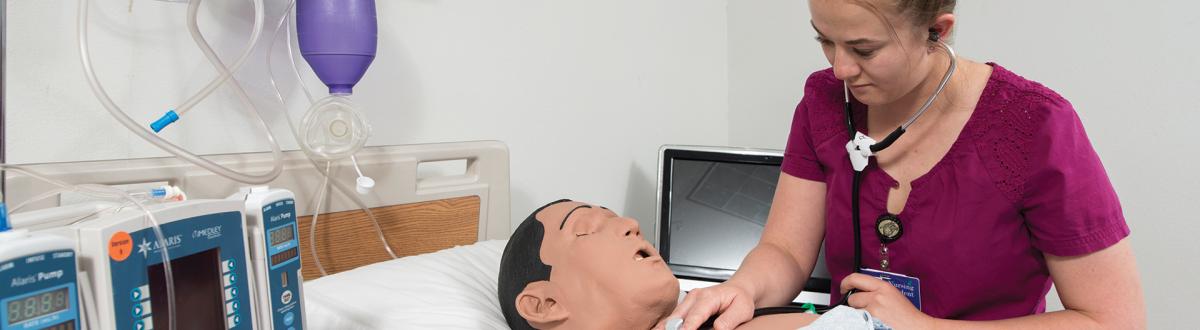 Nursing student using stethoscope on training mannequin