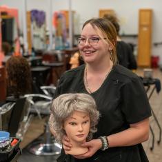 cosmetology student styling wig for local cancer patients