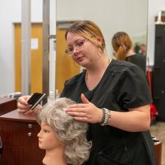 cosmetology student styling wig for local cancer patients